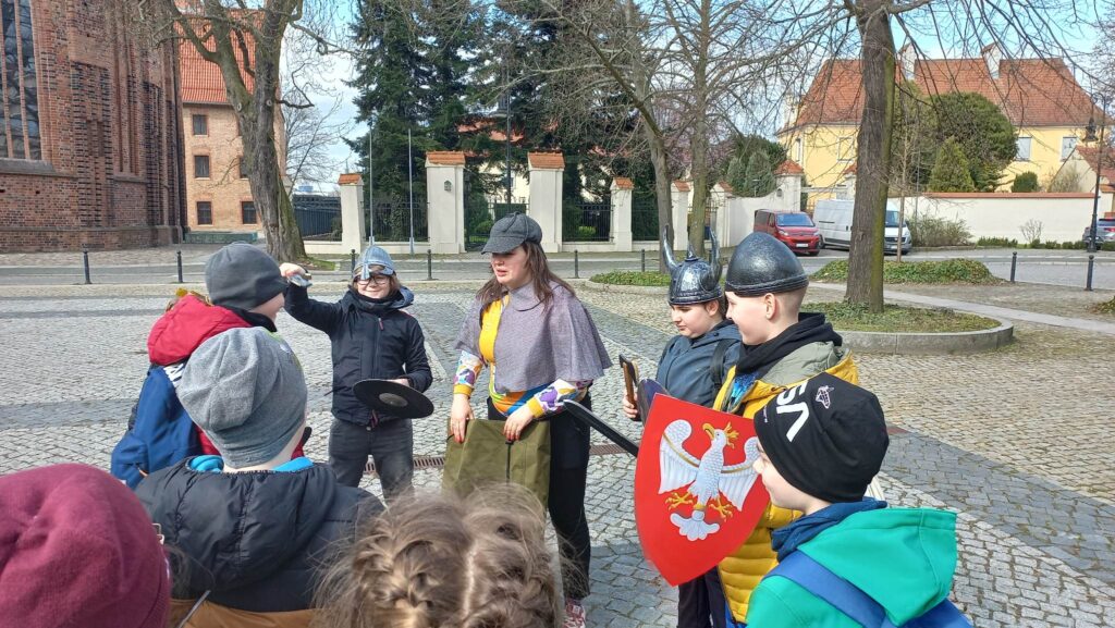 Uczniowie i przewodniczka stoją na placu.