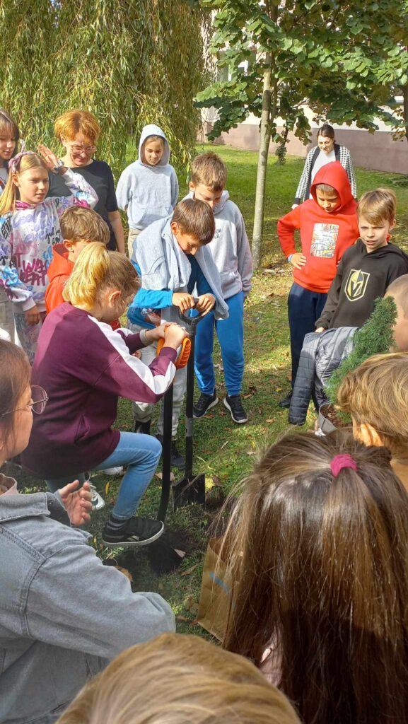 Grupa uczniów na dworze, chłopiec i dziewczynka kopią w ziemi.