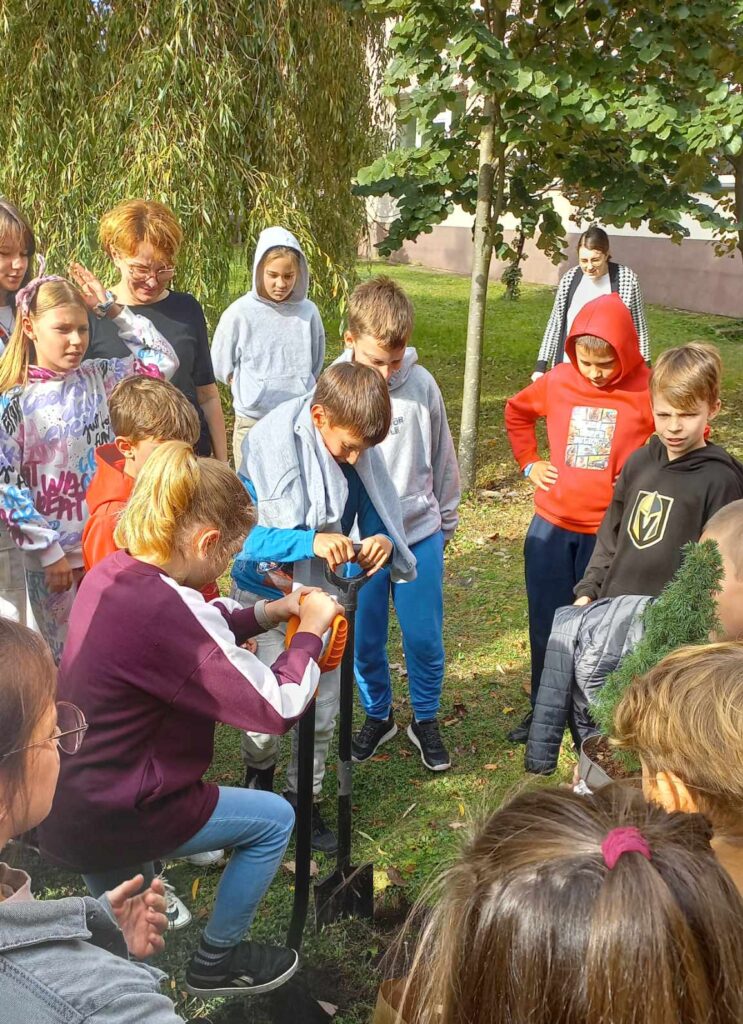 Grupa uczniów na dworze, chłopiec i dziewczynka kopią w ziemi.