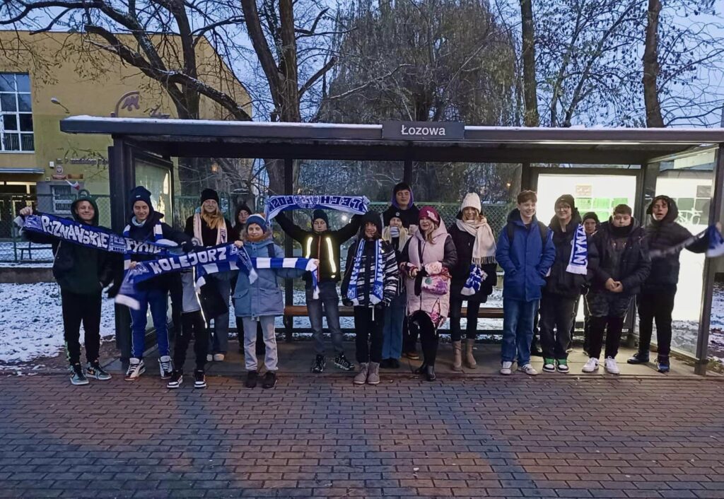 Uczniowie na przystanku tramwajowym z szalikami Lecha.