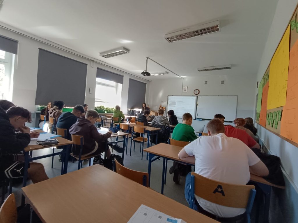 Uczniowie siedzący w ławkach przodem do tablicy.
