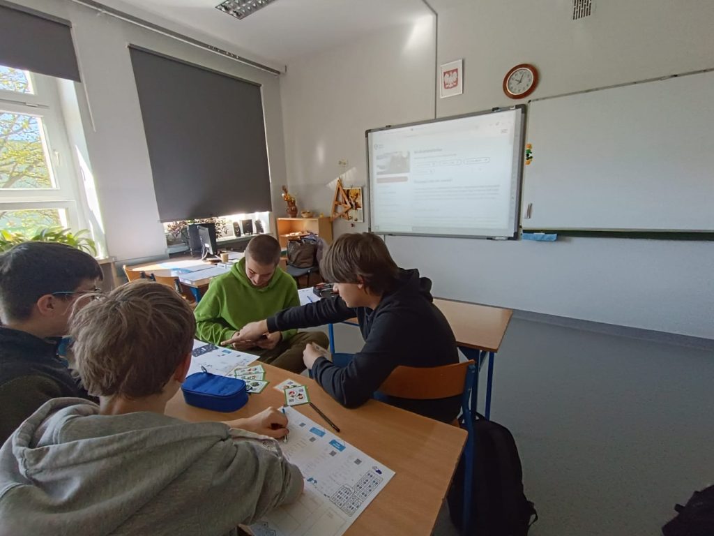 Uczniowie siedzący w ławce i grający w grę karcianą.