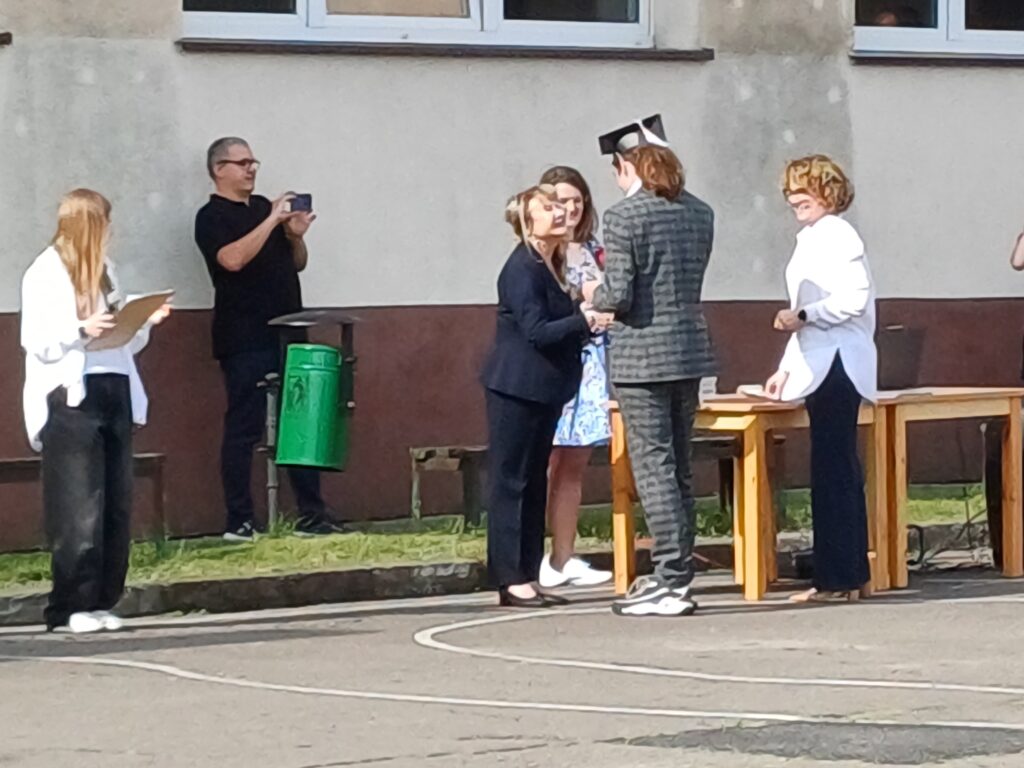 Uczeń odbiera dyplom i gratulacje z rąk nauczycielki.
