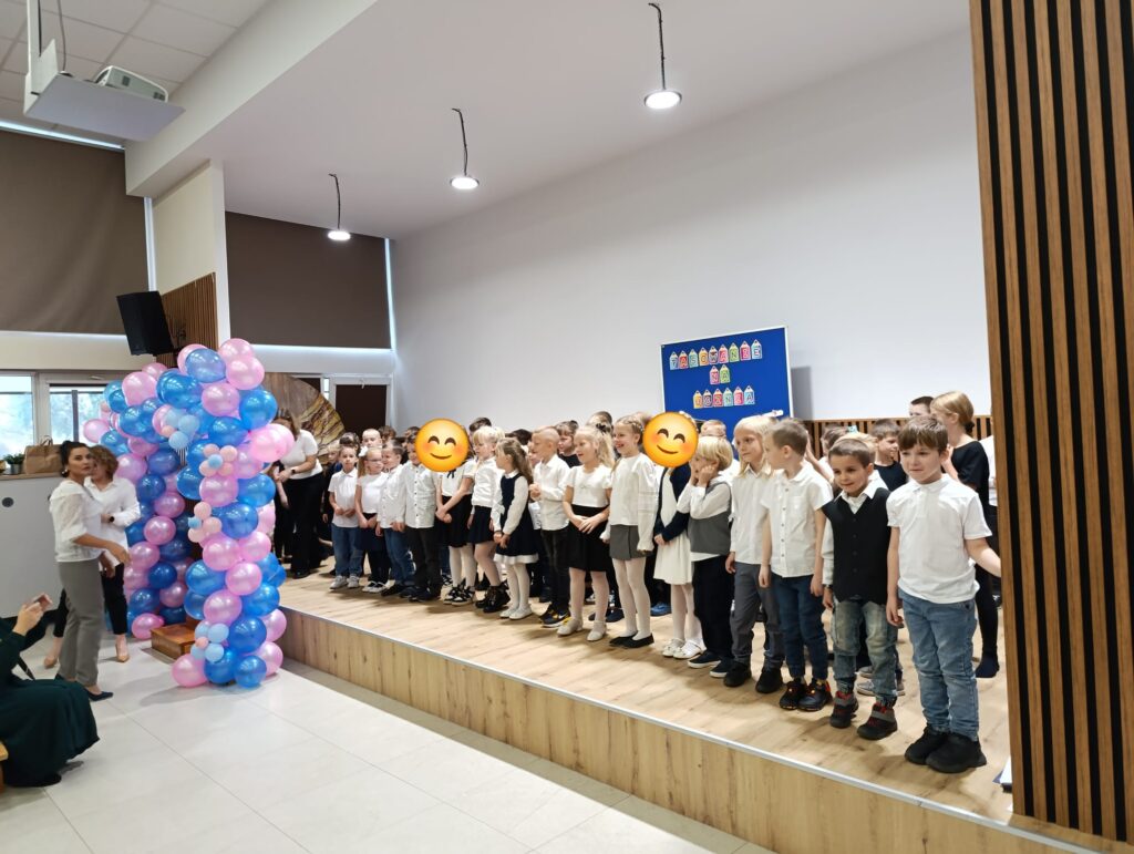 Uczniowie klas pierwszych stojący na scenie w auli.