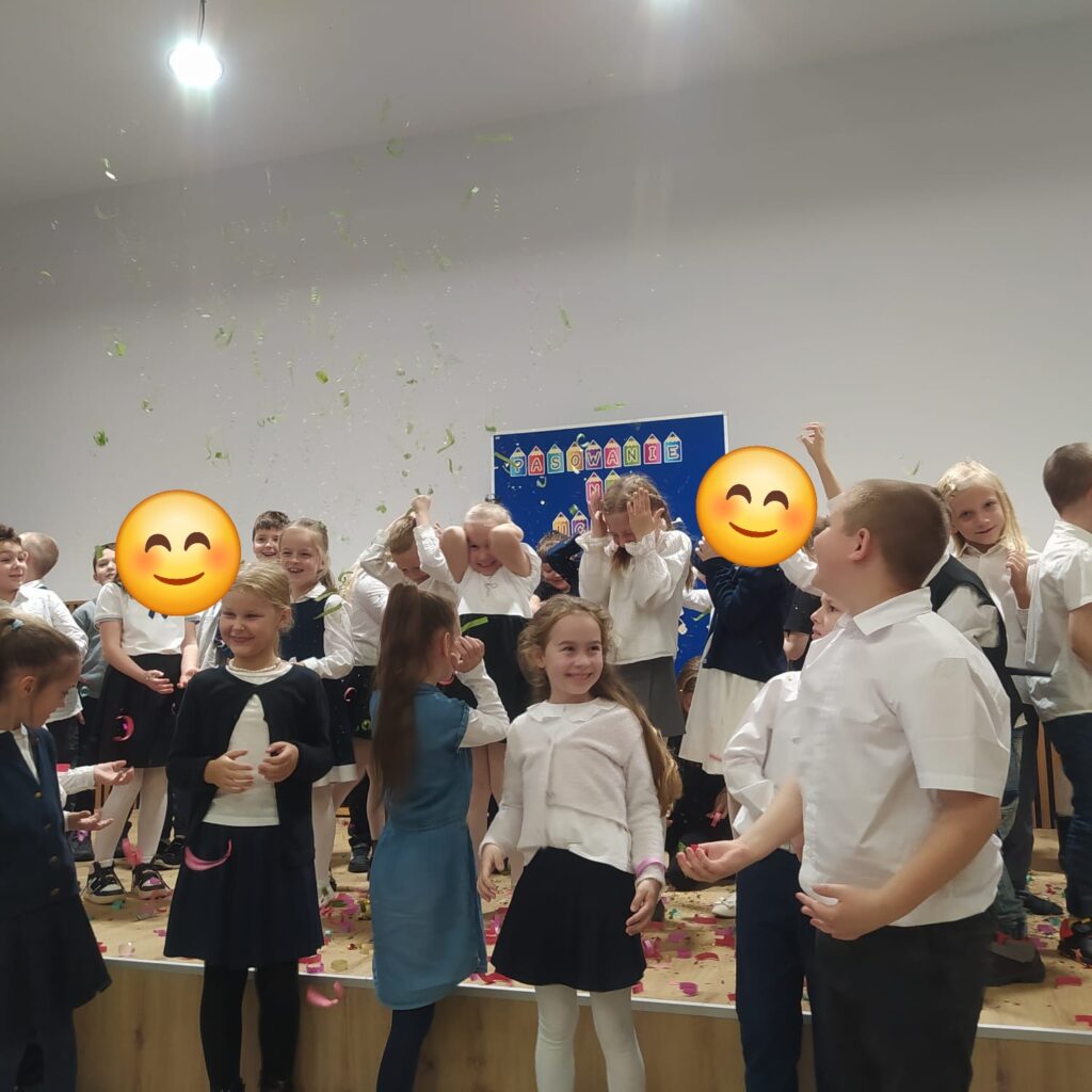 Uczniwoie klas pierwszych stojący na scenie a nad nimi spadające konfetti.