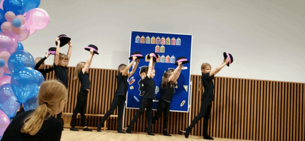 Kilkoro uczniów z klas 1 ubranych na czarno tańczy z kapeluszami trzymanymi nad głowami z wyciągniętymi rękami.