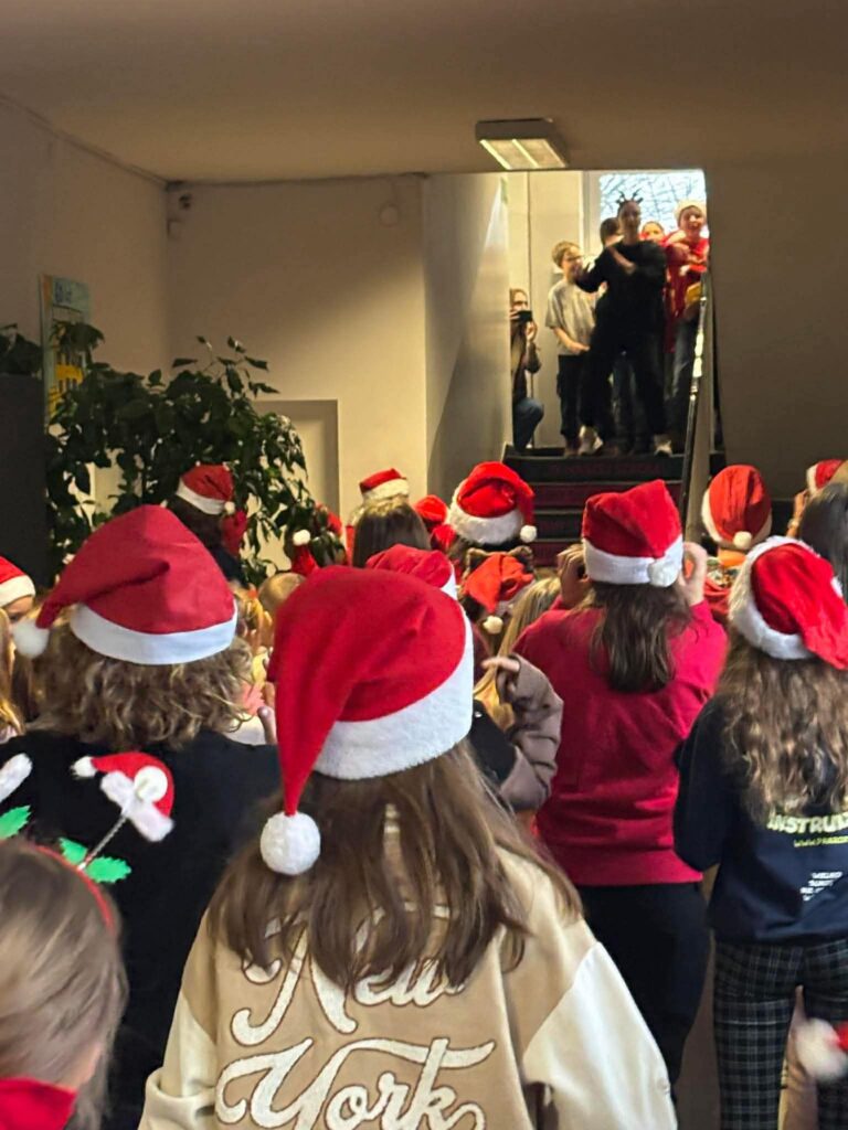 Uczniowie w czapkach Mikołaja na korytarzu szkolnym tańczą.