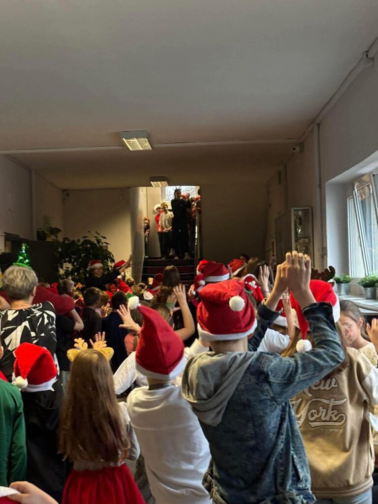 Zdjęcie zrobione od tyłu, uczniowie trzymają ręce w górze i klaszczą.