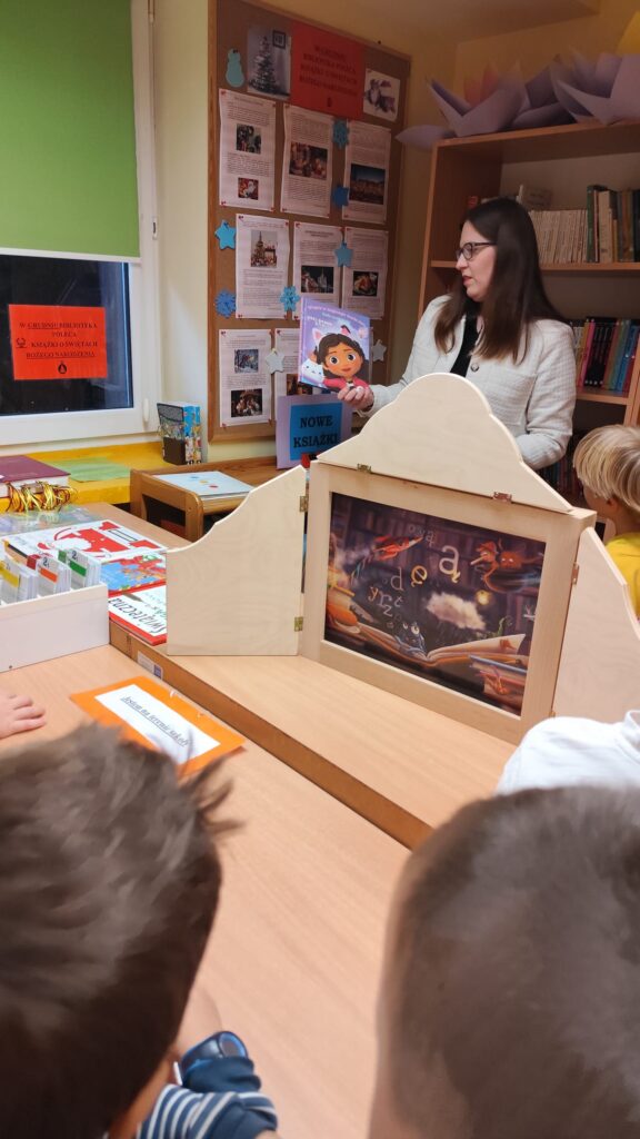 Pani bibliotekarka wystawia przedstawienie "Wypożyczalnia skrzydeł" na biurku leży scena.