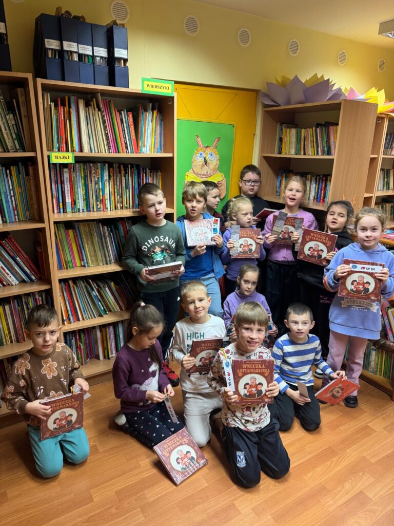Uczniowie klasy pierwszej stojący na tle regałów z książkami