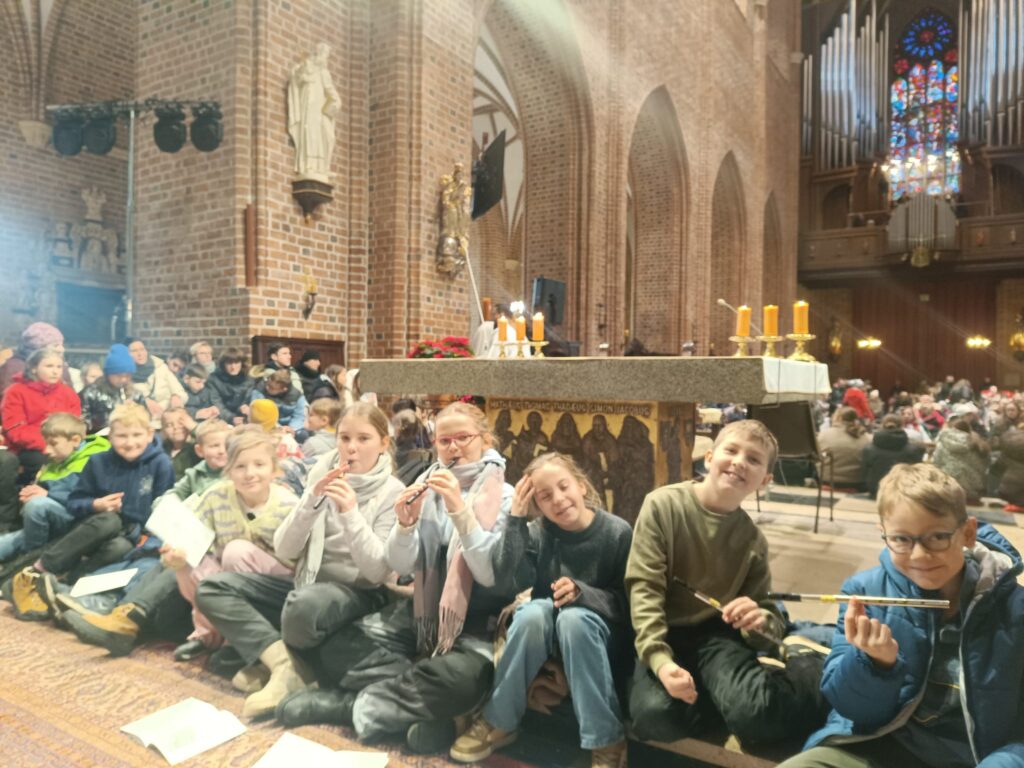 Uczniowie siedzący w Katedrze Poznańskiej i czekający na wspólne kolędowanie.