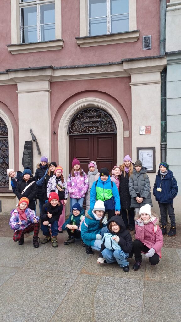 Uczniowie klasy 4b wraz z wychowawczynią na tle drzwi wejściowych budynku.