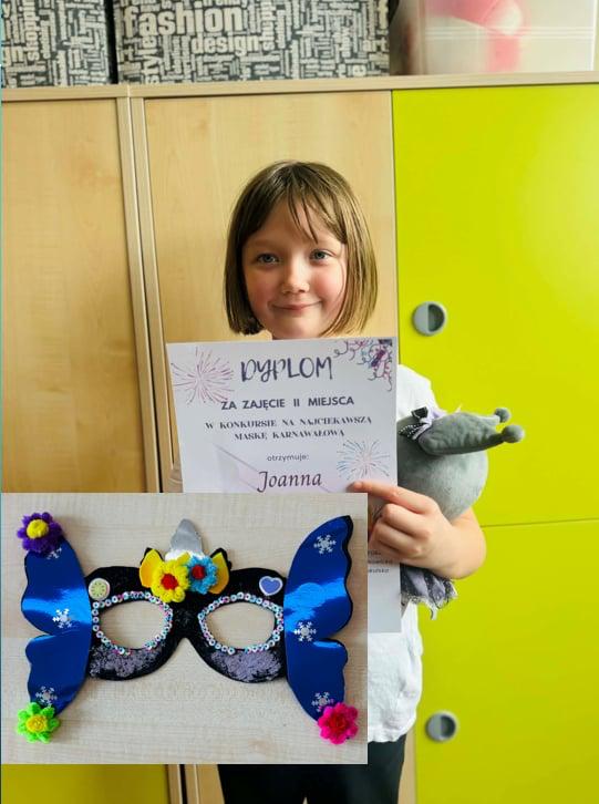 Uczennica trzymająca dyplom i nagrodę stojąca na tle szafek.