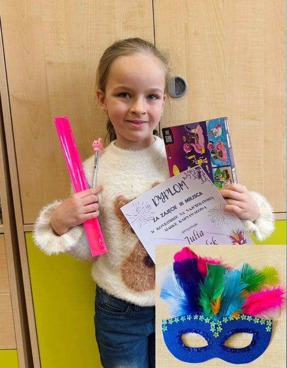 Uczennica trzymająca dyplom wraz z nagrodą stojąca na tle szafy.