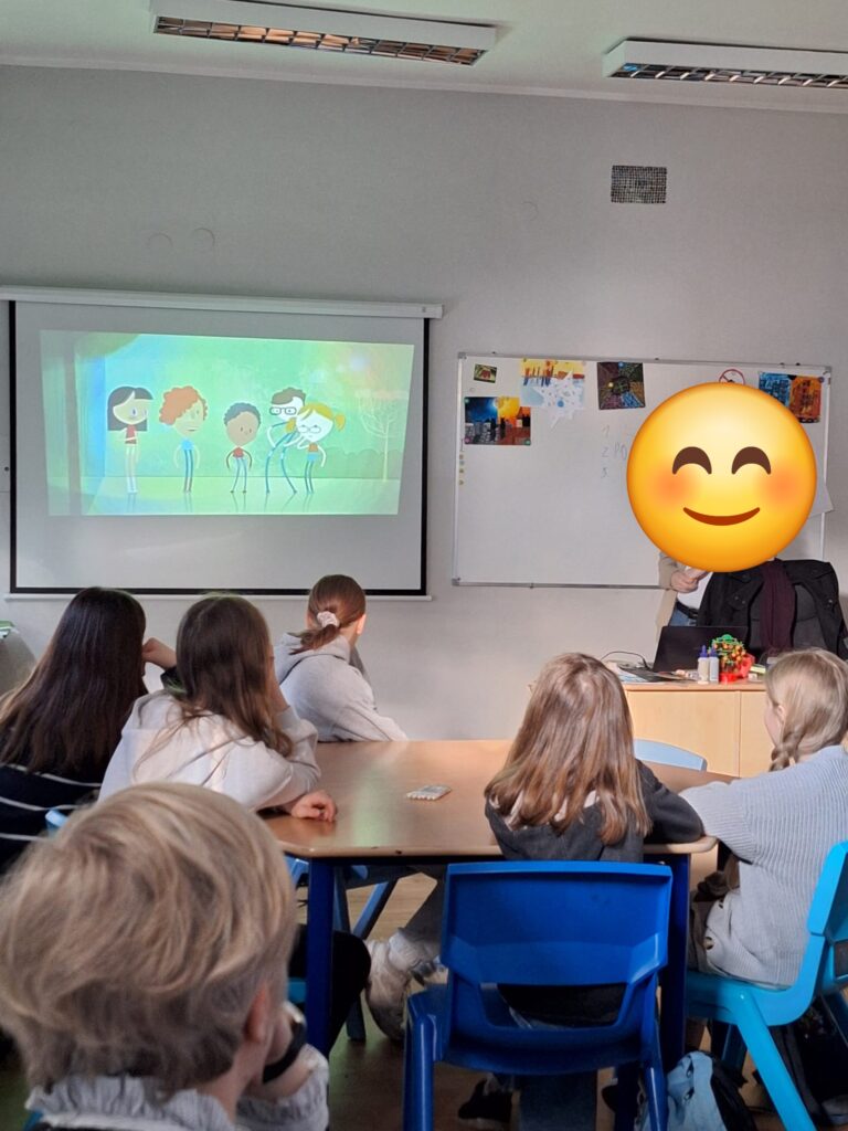 Uczniowie siedzący w ławkach oglądający animację na tablicy multimedialnej.