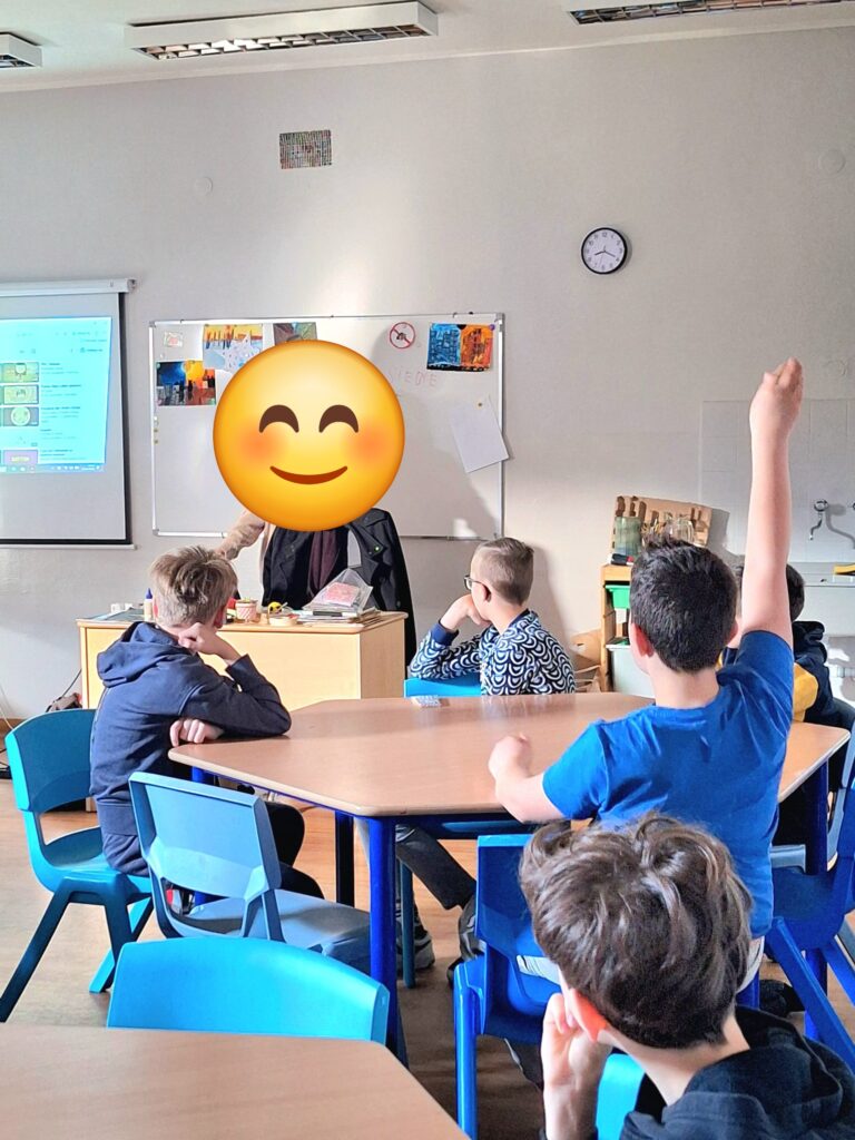 Uczniowie siedzący w ławkach oglądajacy film animacyjny, jeden uczeń zgłasza się poprzez podniesienie ręki.