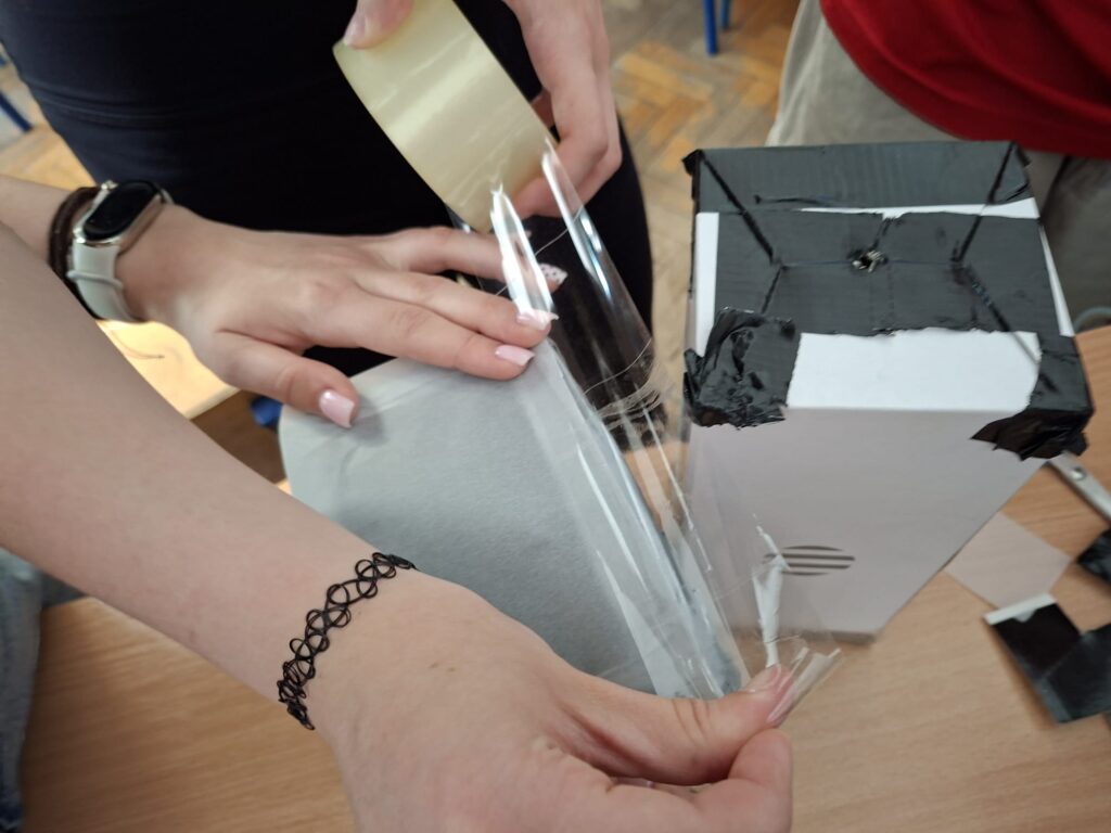 Kamera obscura jest tworzona przez uczniów, na zdjęciu kleją elementy 